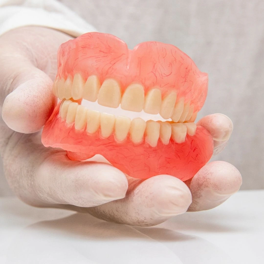 A full set of upper and lower dentures held in a gloved hand